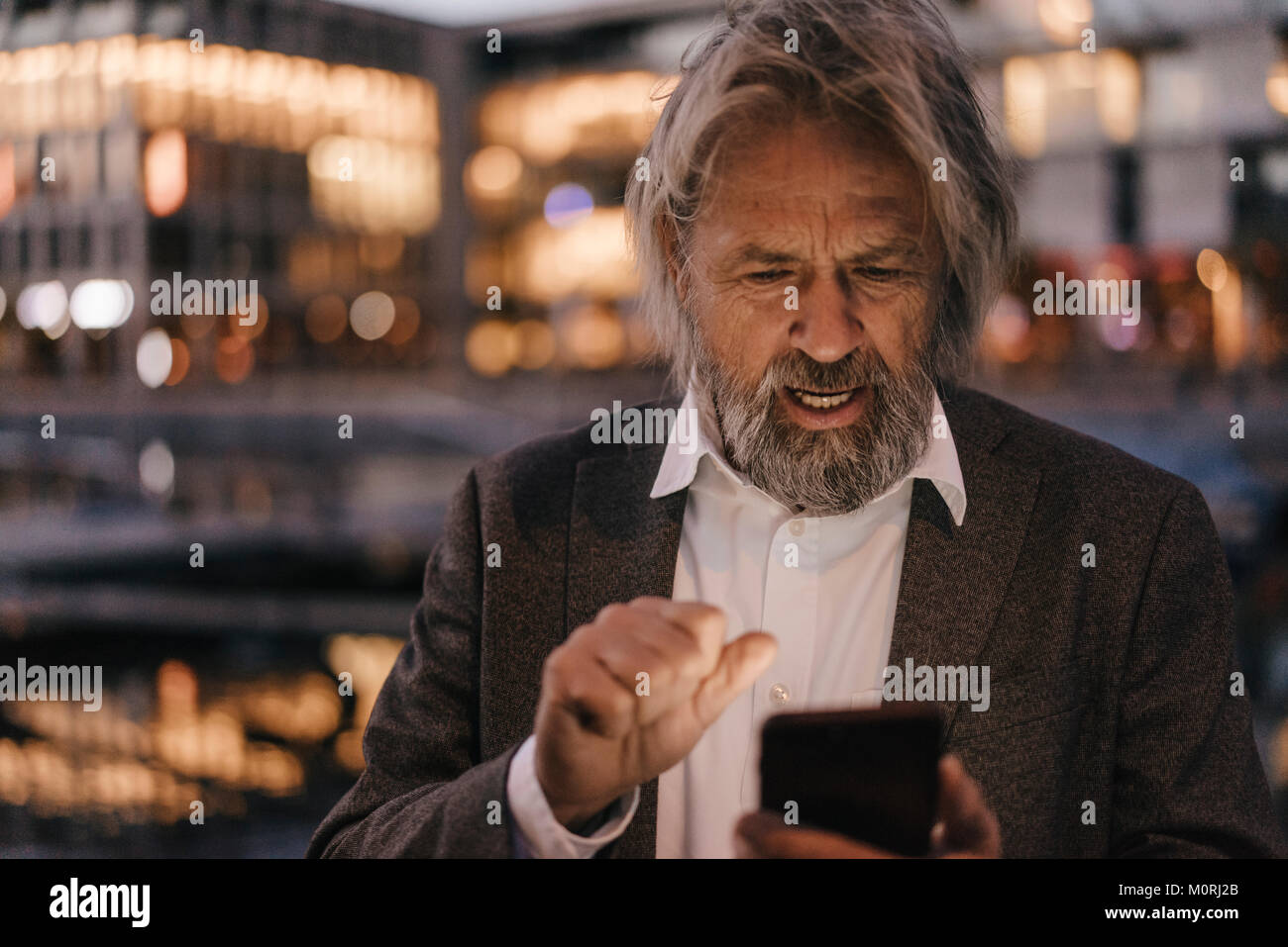 Senior man using cell phone outdoors at dusk Stock Photo - Alamy