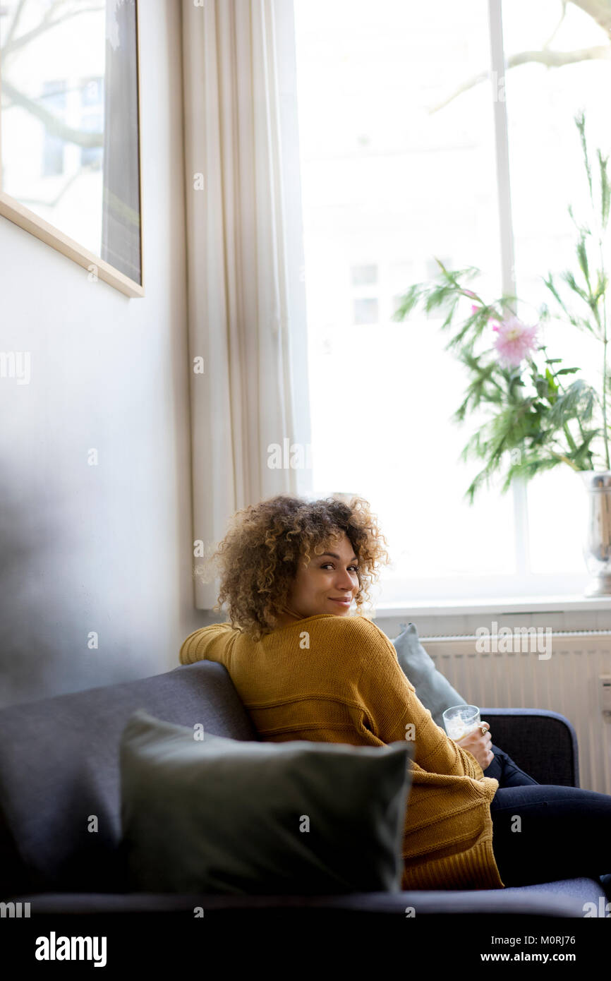 Portrait of smiling young woman sitting on couch at home Stock Photo ...