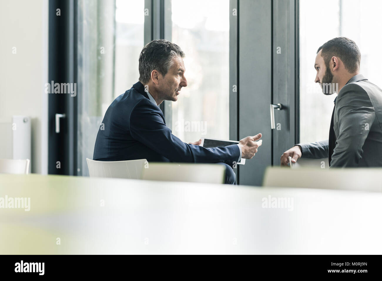 Two businessmen talking in office at the window Stock Photo - Alamy