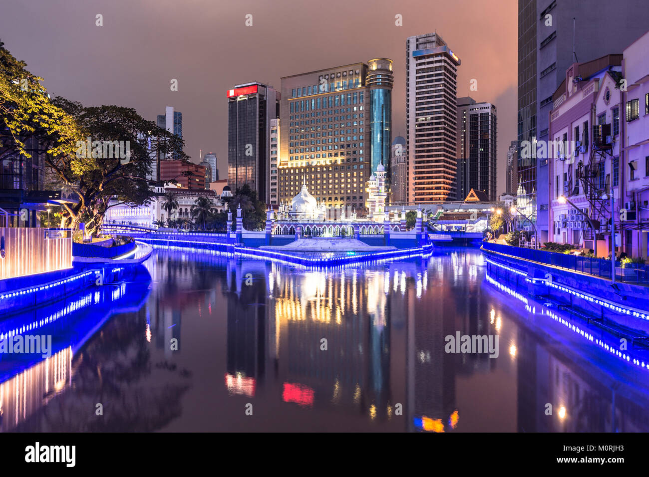 Office buildings reflect in the water of the Klang river in front of the Jamek mosque (masjid) in the heart of Kuala Lumpur in Malaysia at night. The  Stock Photo