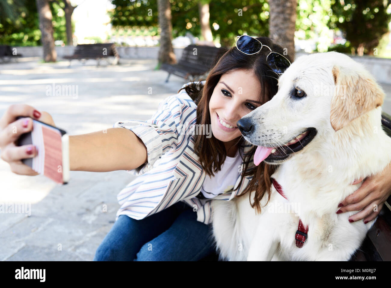 Young pretty girl and Golden dog taking a self-portrait with her phone in urban environment in summer. Stock Photo