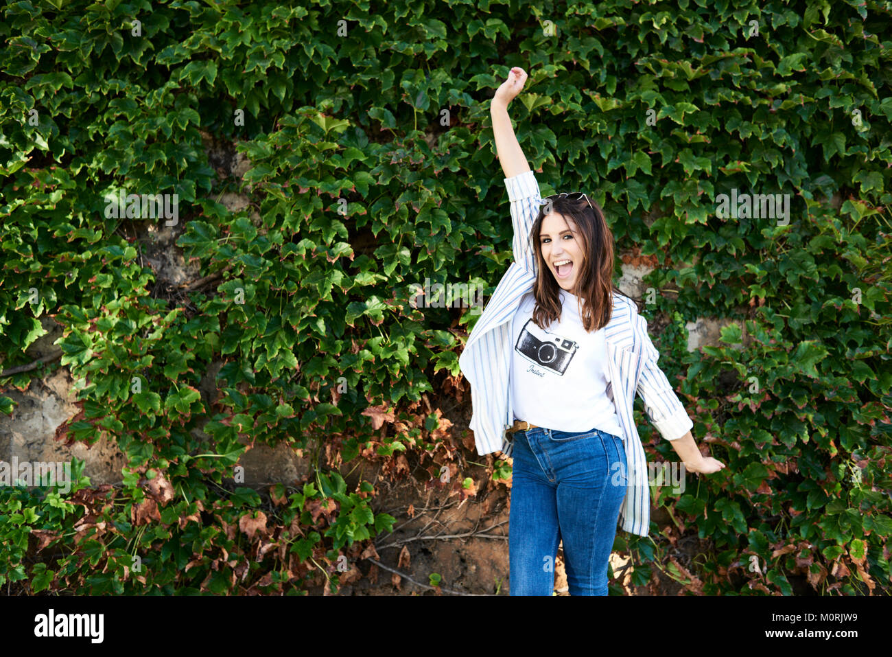 Happy millennial girl moving freely against garden wall in summer. Stock Photo