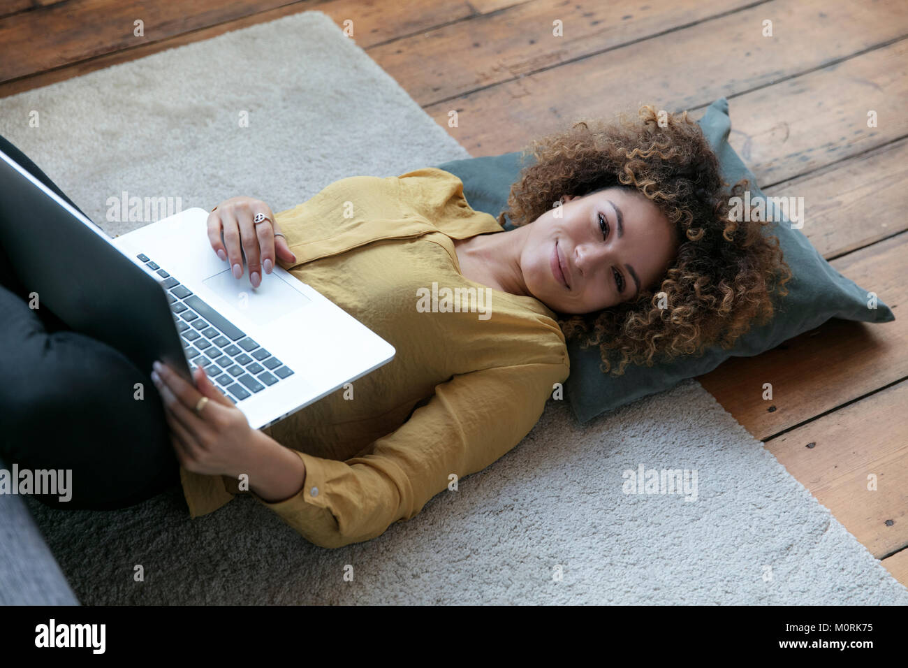 Smiling young woman lying on the floor at home with laptop Stock Photo ...