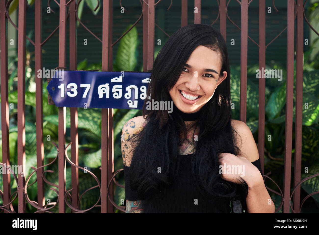 Portrait of a happy tattooed asian girl against tropical plant in the background. Stock Photo