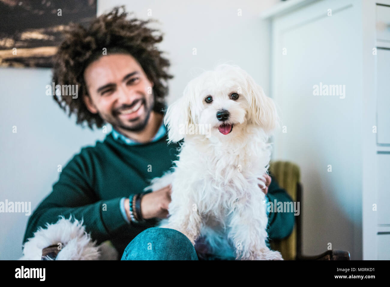 Cute little white dog sitting on lap of his happy owner Stock Photo