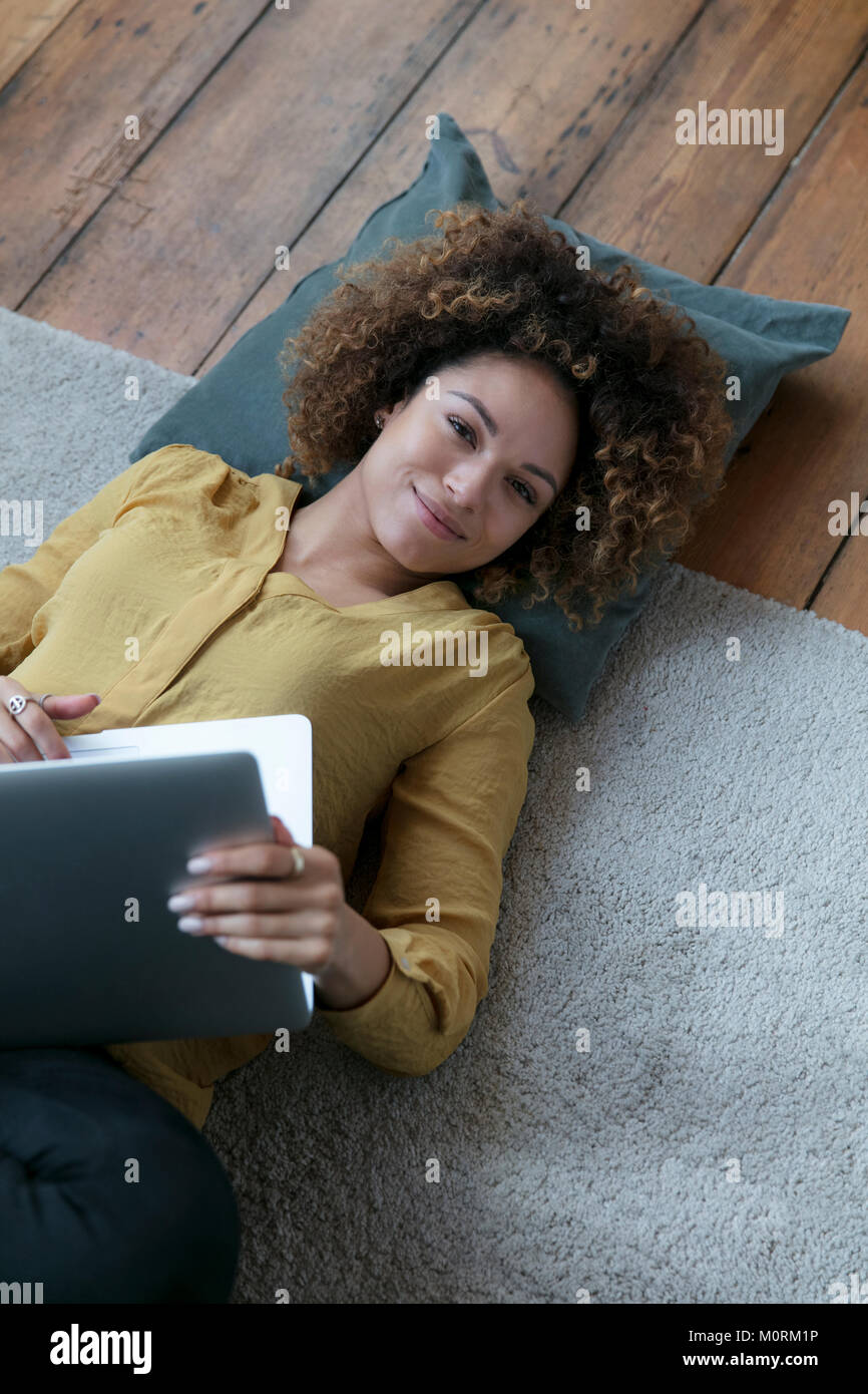 Smiling young woman lying on the floor at home with laptop Stock Photo ...
