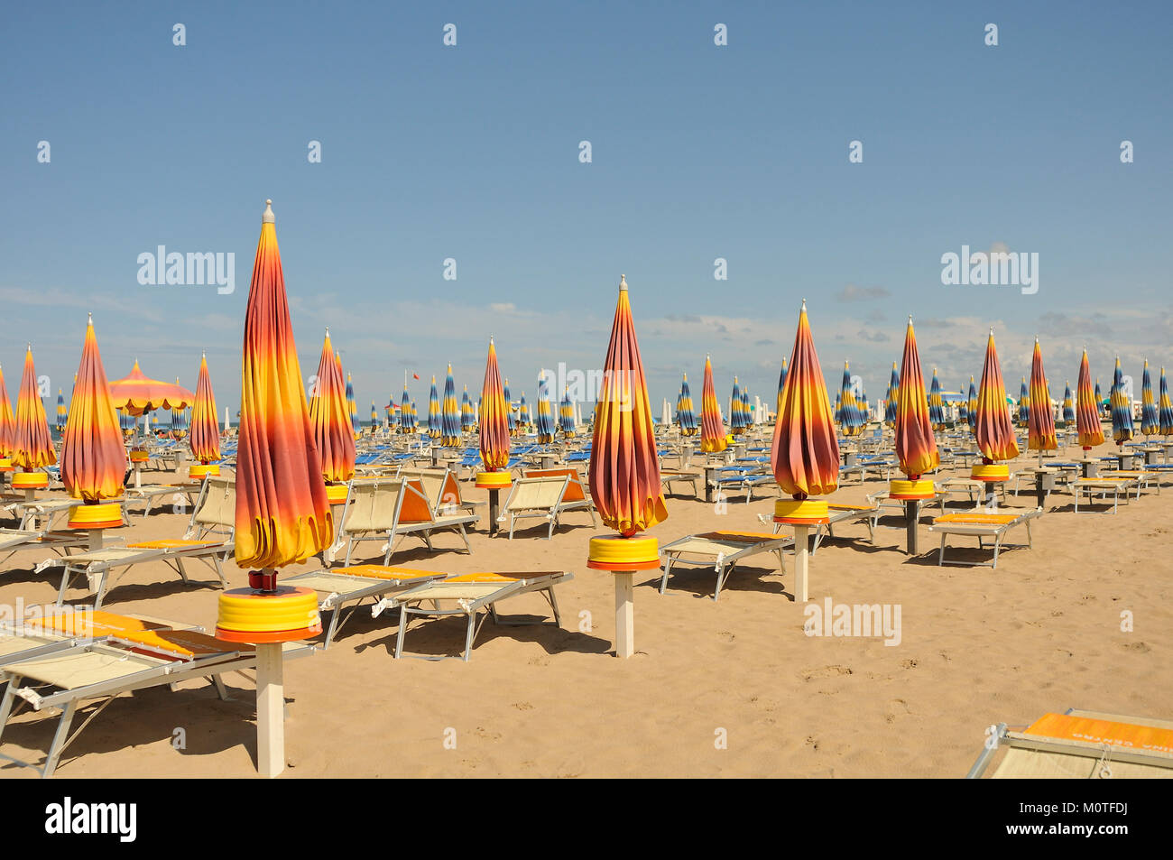 Closed beach parasol umbrellas on the beach at Rimini, Italy Stock Photo -