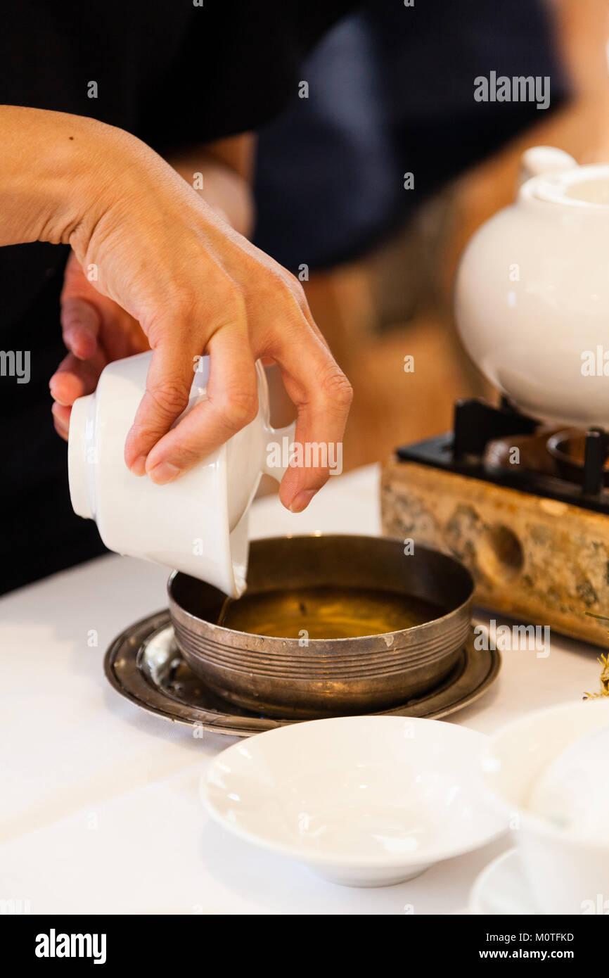 Steeping Chinese tea leaves by pouring excess water into bronze container as part of brewing tea during traditional dim sum meal. Stock Photo