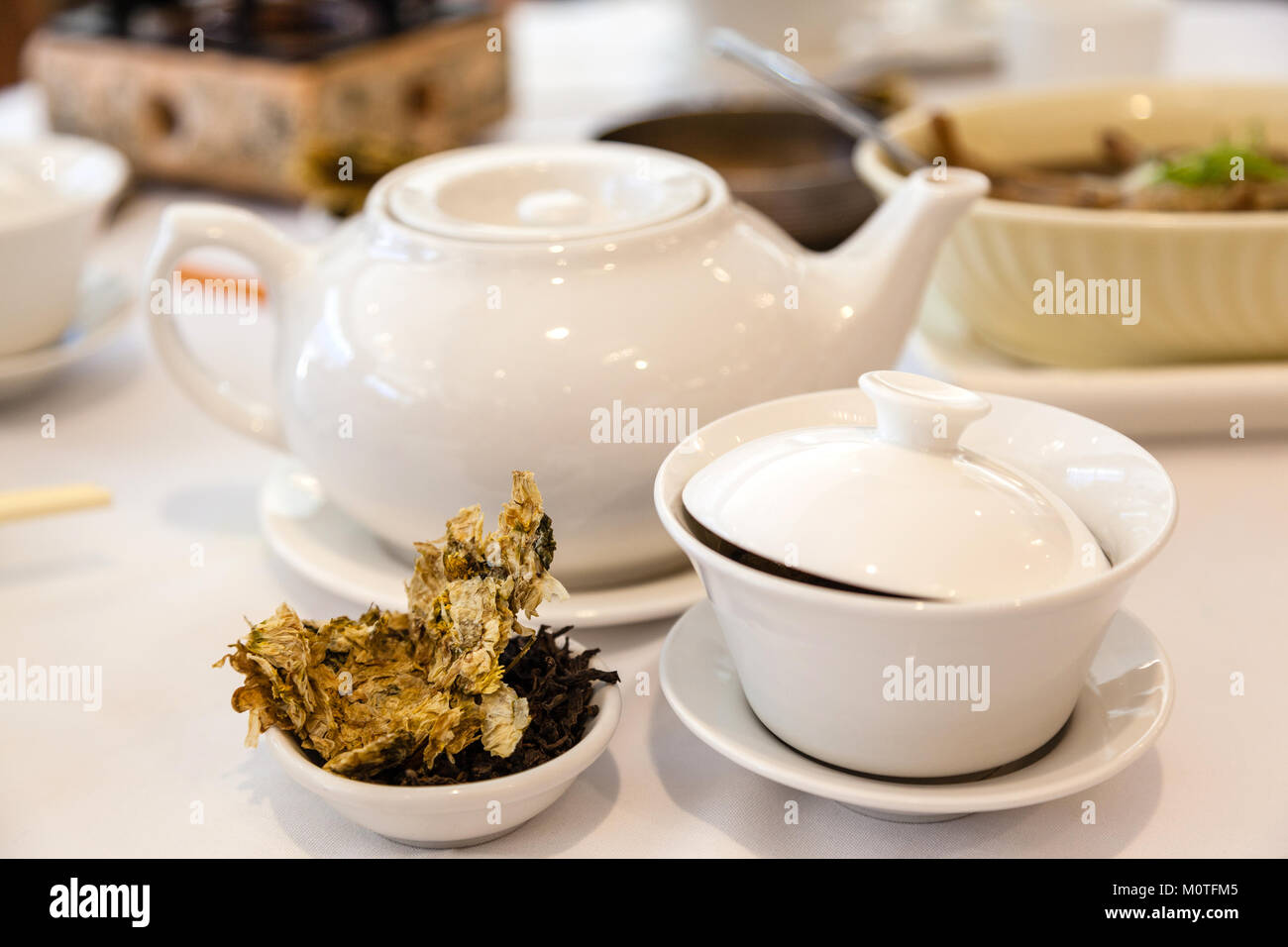 Brewing Chinese tea for dim sum meal with tea leaves and traditional tea cup in the foreground. Stock Photo
