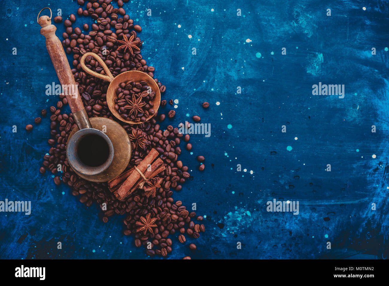 ?opper cezve on scattered coffee beans with handmaiden wooden scoop, cinnamon and anise stars on a dark background. Creative coffee ingredients flat l Stock Photo