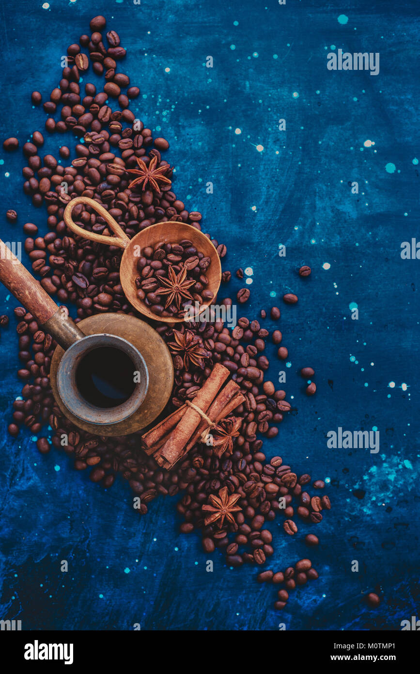 ?opper cezve on scattered coffee beans with handmaiden wooden scoop, cinnamon and anise stars on a dark background. Top view hot drink photography wit Stock Photo
