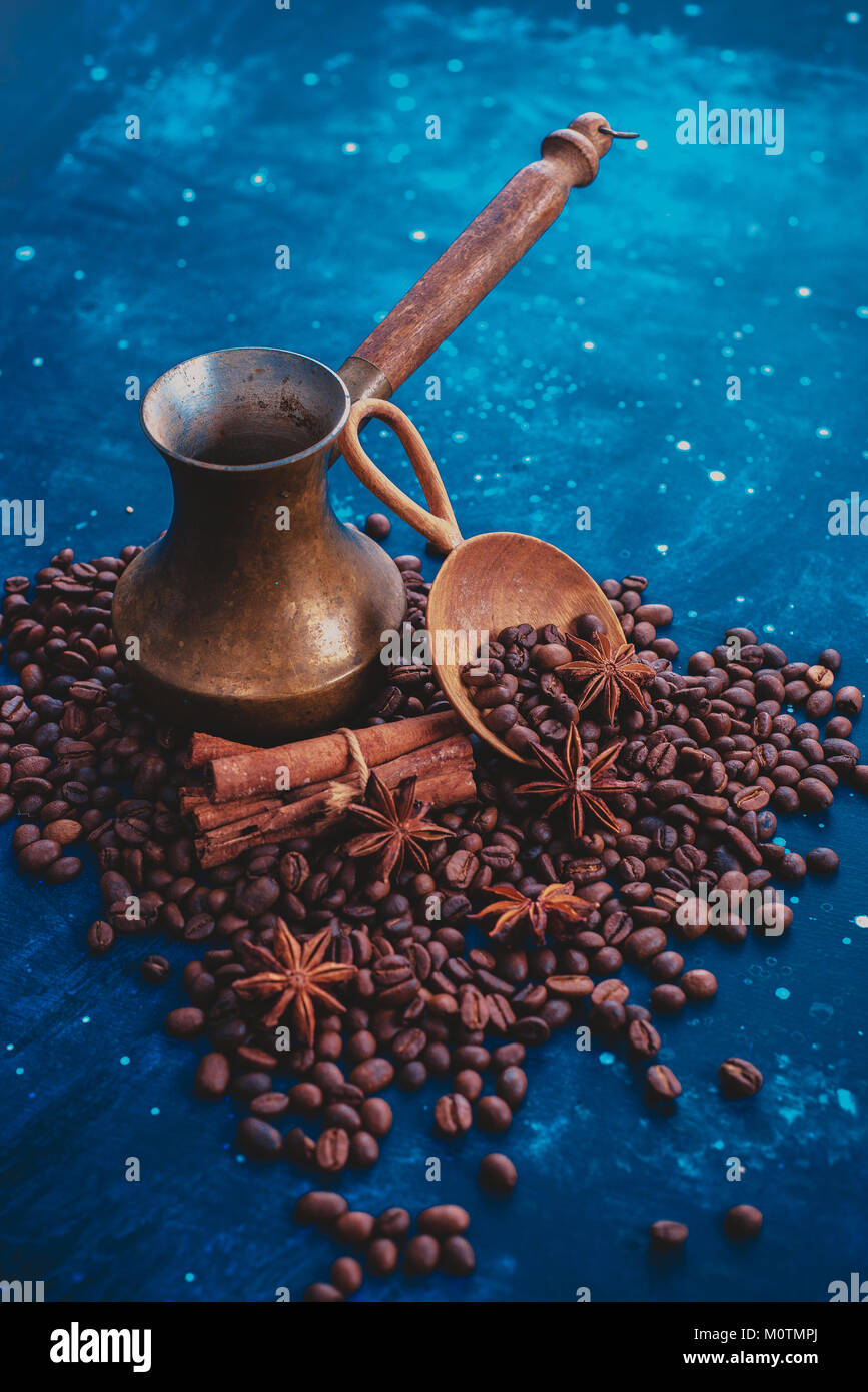 ?opper cezve on scattered coffee beans with handmaiden wooden scoop, cinnamon and anise stars on a dark background. Dark food photography with copy sp Stock Photo