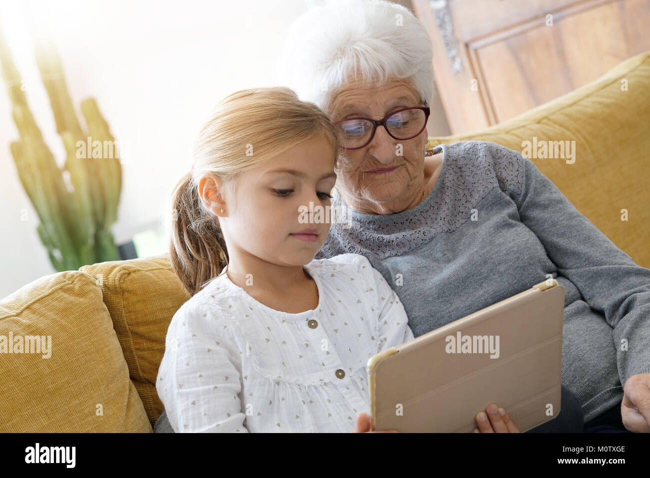 Little girl with grandmother using tablet at home Stock Photo - Alamy