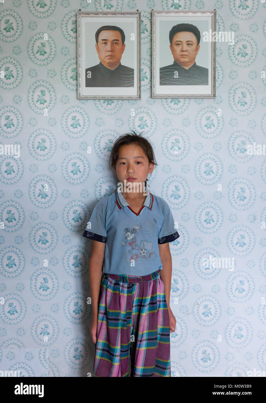 North Korean girl posing below the portraits of the Dear Leaders inside her home, Kangwon Province, Chonsam Cooperative Farm, North Korea Stock Photo