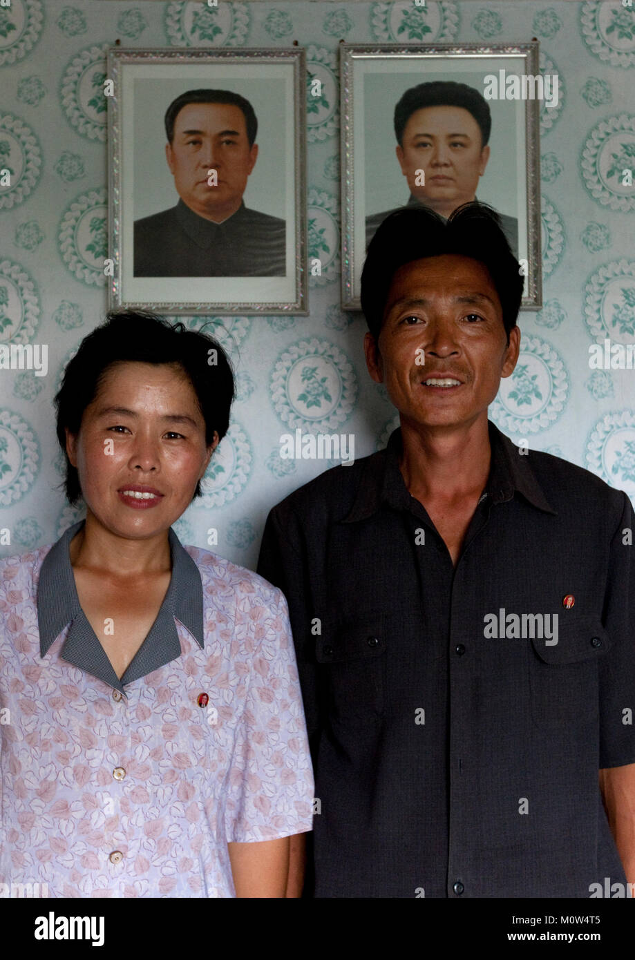 Smiling North Korean couple in front of the official portraits of the Dear Leaders in their house, Kangwon Province, Chonsam Cooperative Farm, North Korea Stock Photo