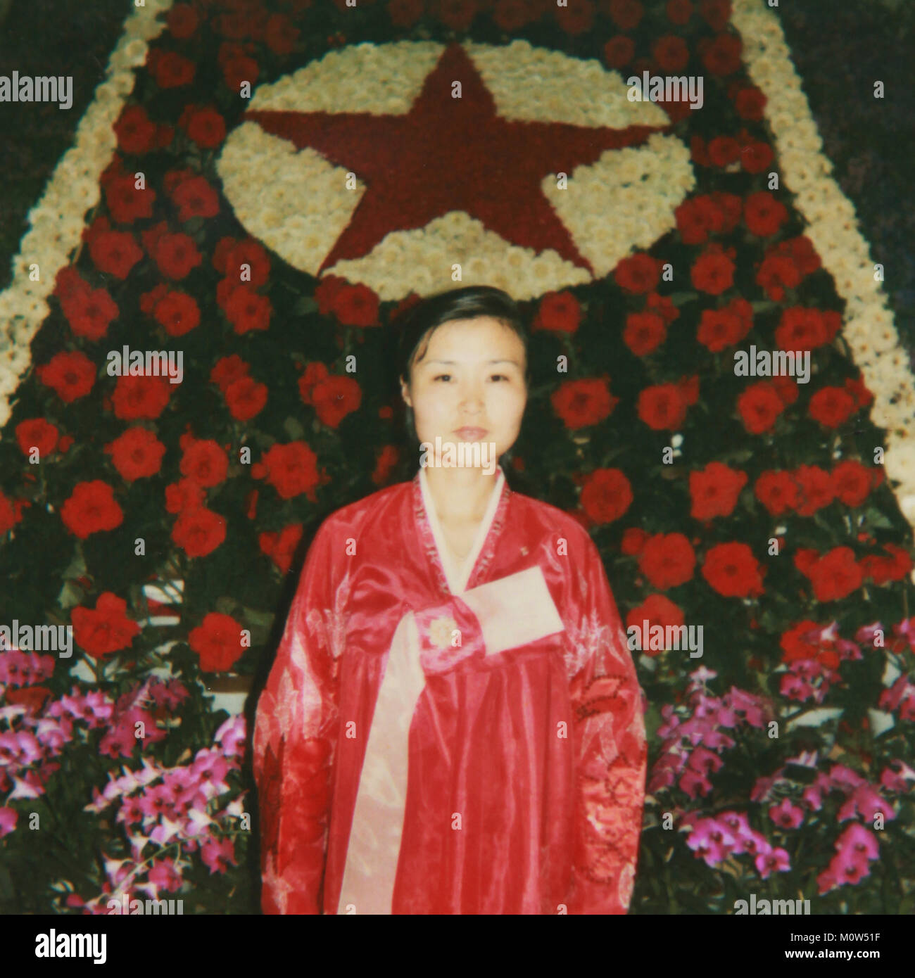 Polaroid of a woman posing in front of a red star made of Kimjongilia flowers during the international Kimilsungia and Kimjongilia festival, Pyongan Province, Pyongyang, North Korea Stock Photo