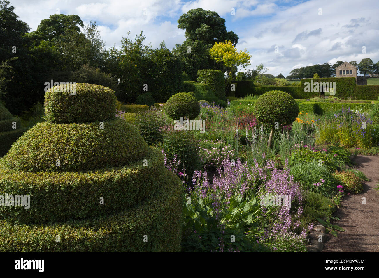 Topiary and colourful herbaceous borders of the Flower Garden with a summerhouse in the background, Herterton House gardens, Northumberland, England Stock Photo