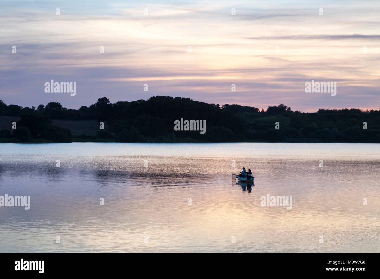 A pair of anglers fishing for Trout from a wooden motor boat on Ravensthorpe reservoir in late September after sunset, Northamptonshire, England. Stock Photo