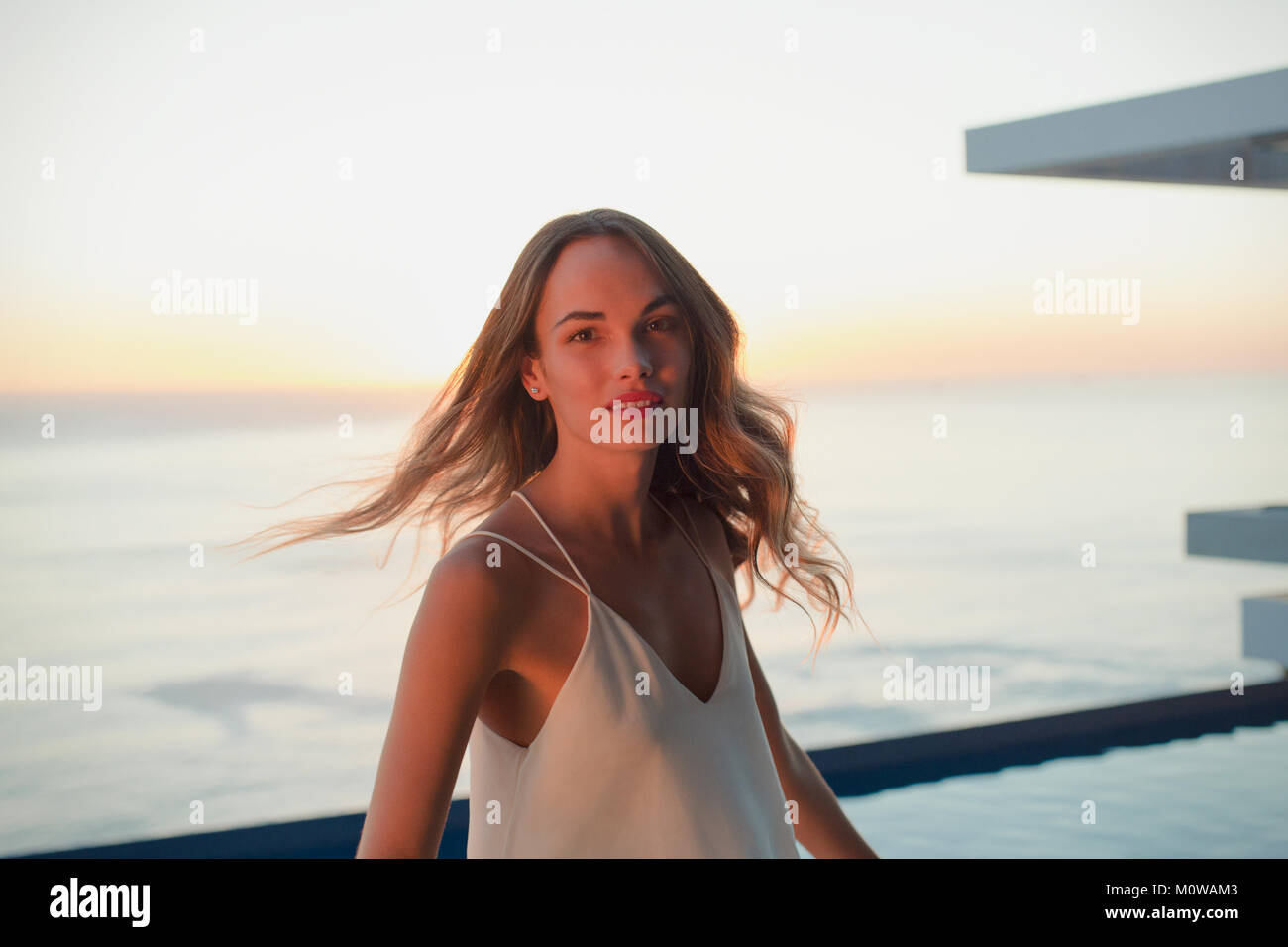 Portrait confident woman turning on luxury balcony with sunset ocean view Stock Photo