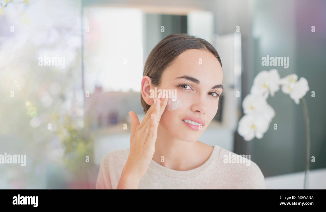 Portrait brunette woman applying face moisturizer to cheek Stock Photo