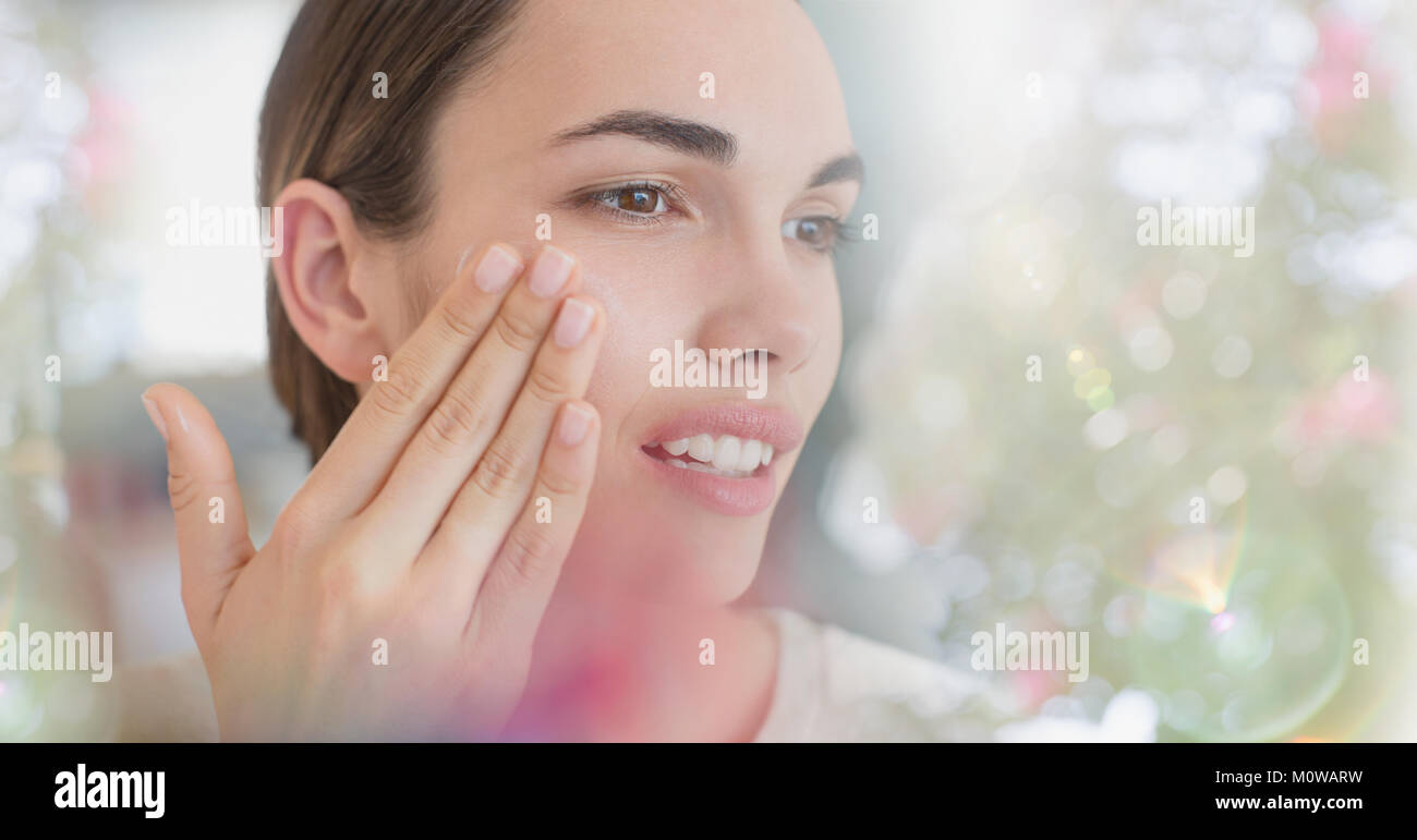 Brunette woman applying face moisturizer to cheek Stock Photo