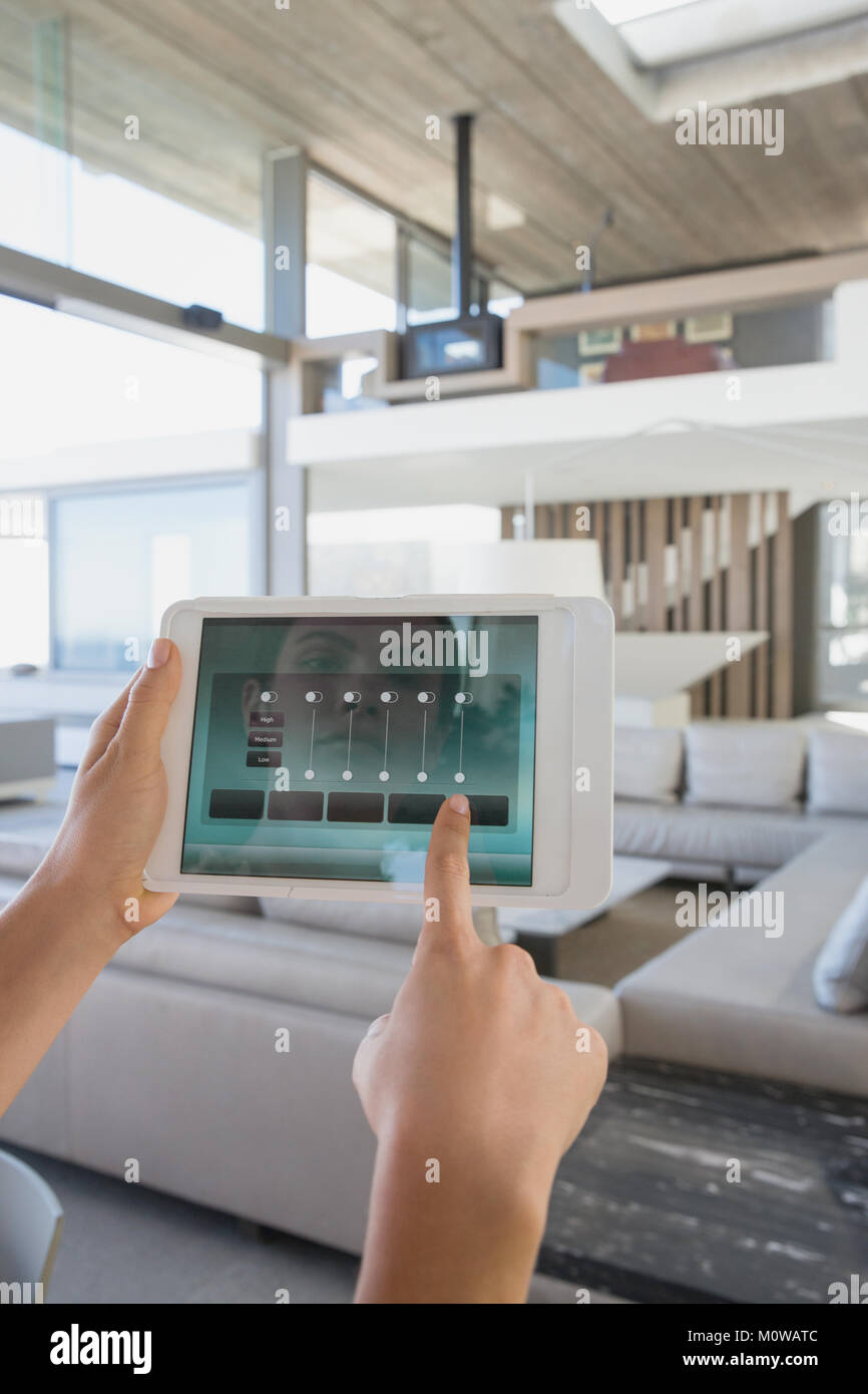 Personal perspective woman with digital tablet setting digital climate control in modern, luxury home showcase interior living room Stock Photo