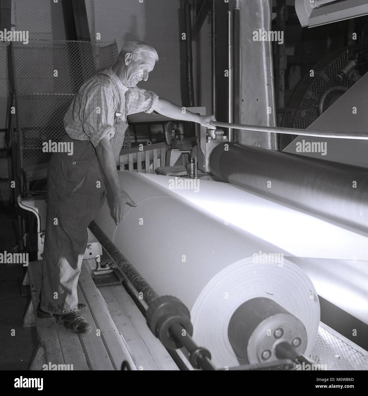 1950s, historical, male worker using a large paper making machine with giant rollers, on which the newly processed paper feeds onto, England, UK. Stock Photo