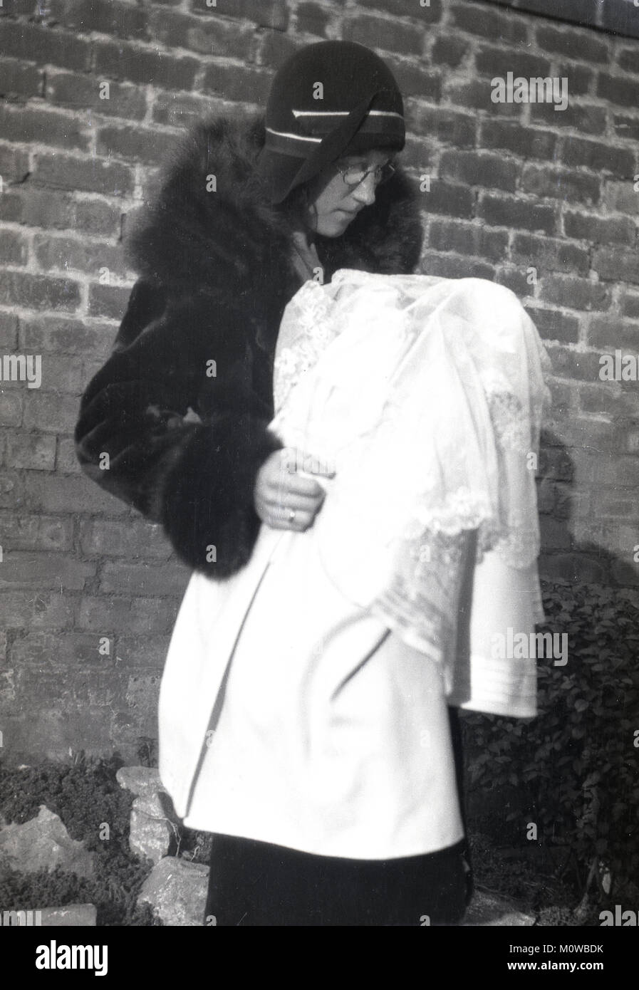 @1920s, historical picture of a happy new mother outside wearing a coat and hat of the period holding her baby covered or swathed with a large shawl, England, UK. Stock Photo