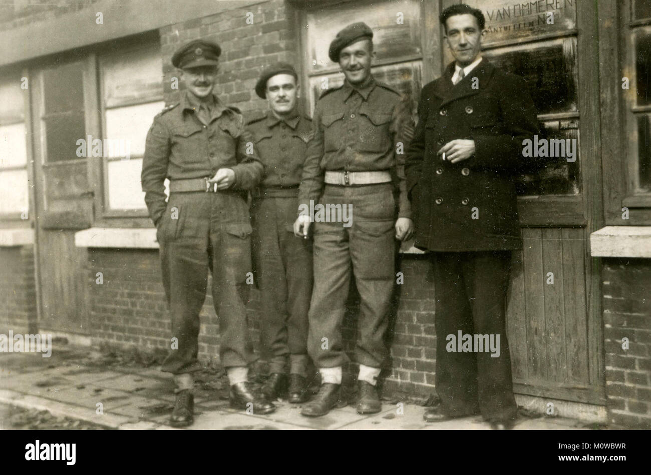 1944, historical, WW2, Ghent, Belguim, three British army officers standing outiside a building with a local civilian enjoying a cigarette. Stock Photo