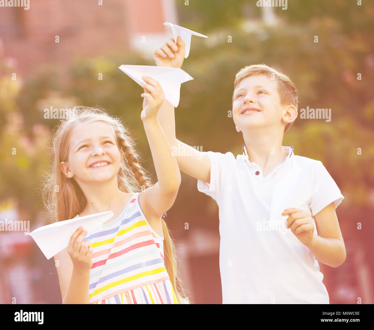 two happy kids playing with simple paper planes on sunny day in town ...