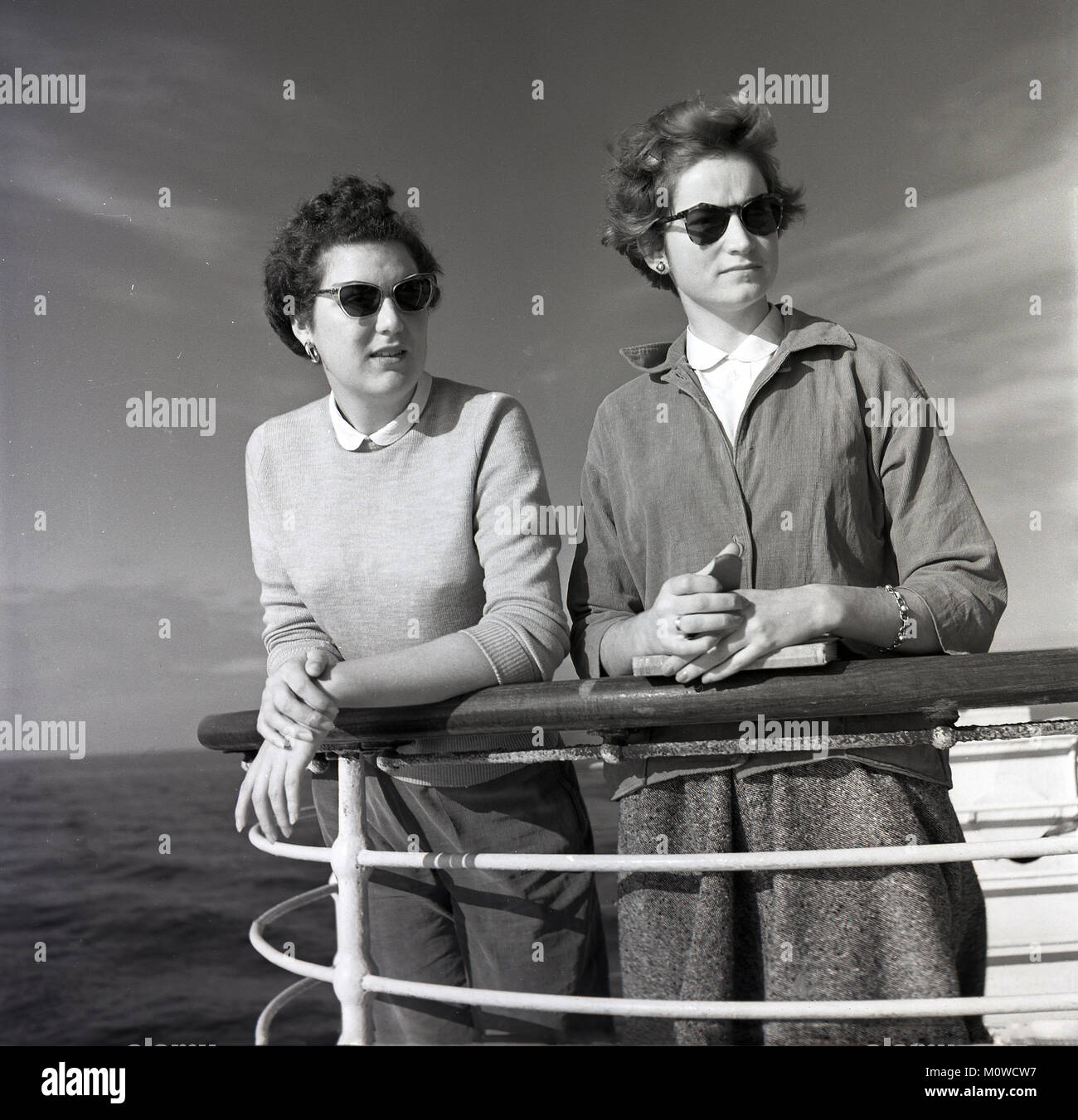 1950s, historical picture of two young woman leaning on a railing or handrail on the deck of a Union-Castle steamship as they look out over the ocean as the ship sails for the Cape in South Africa. These steamships took cargo, mail and passengers overseas with many of those on board going to start a new life away from the gloom of post-war Britain Stock Photo