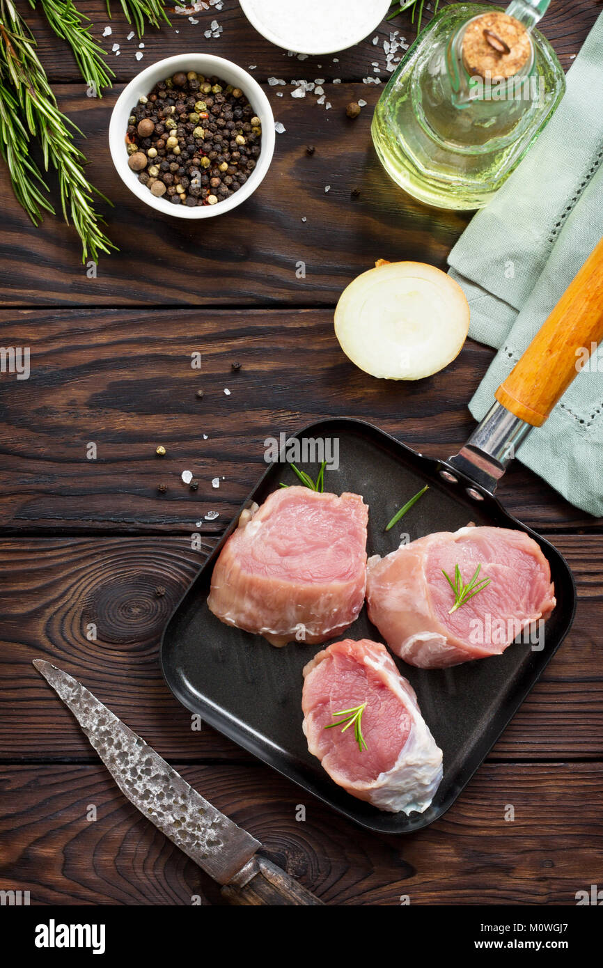 Fresh meat. Raw pork steak on a cast iron frying pan, spices and fresh rosemary on a kitchen wooden table. Stock Photo