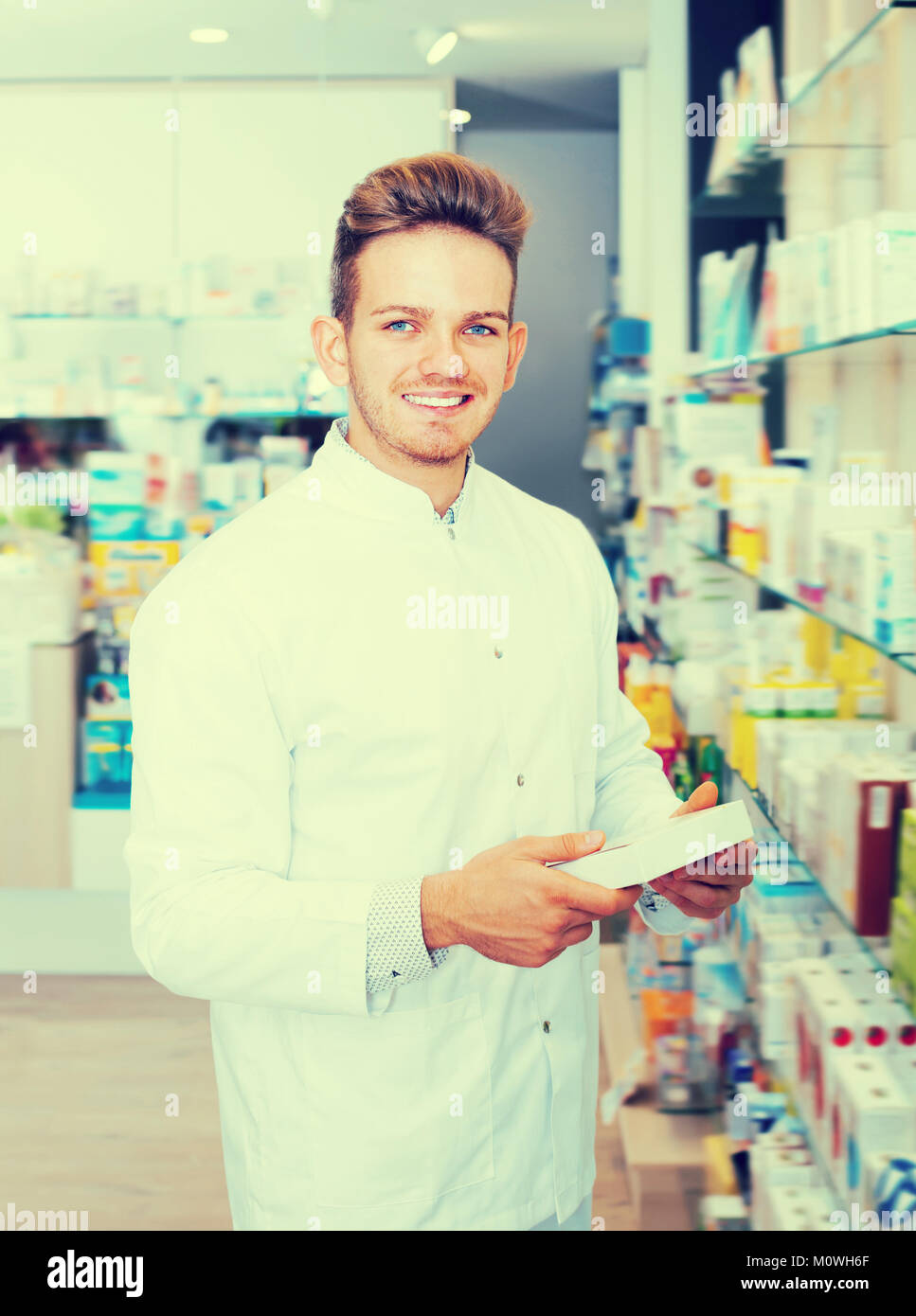 Adult man pharmacist wearing white coat standing among shelves in drug ...