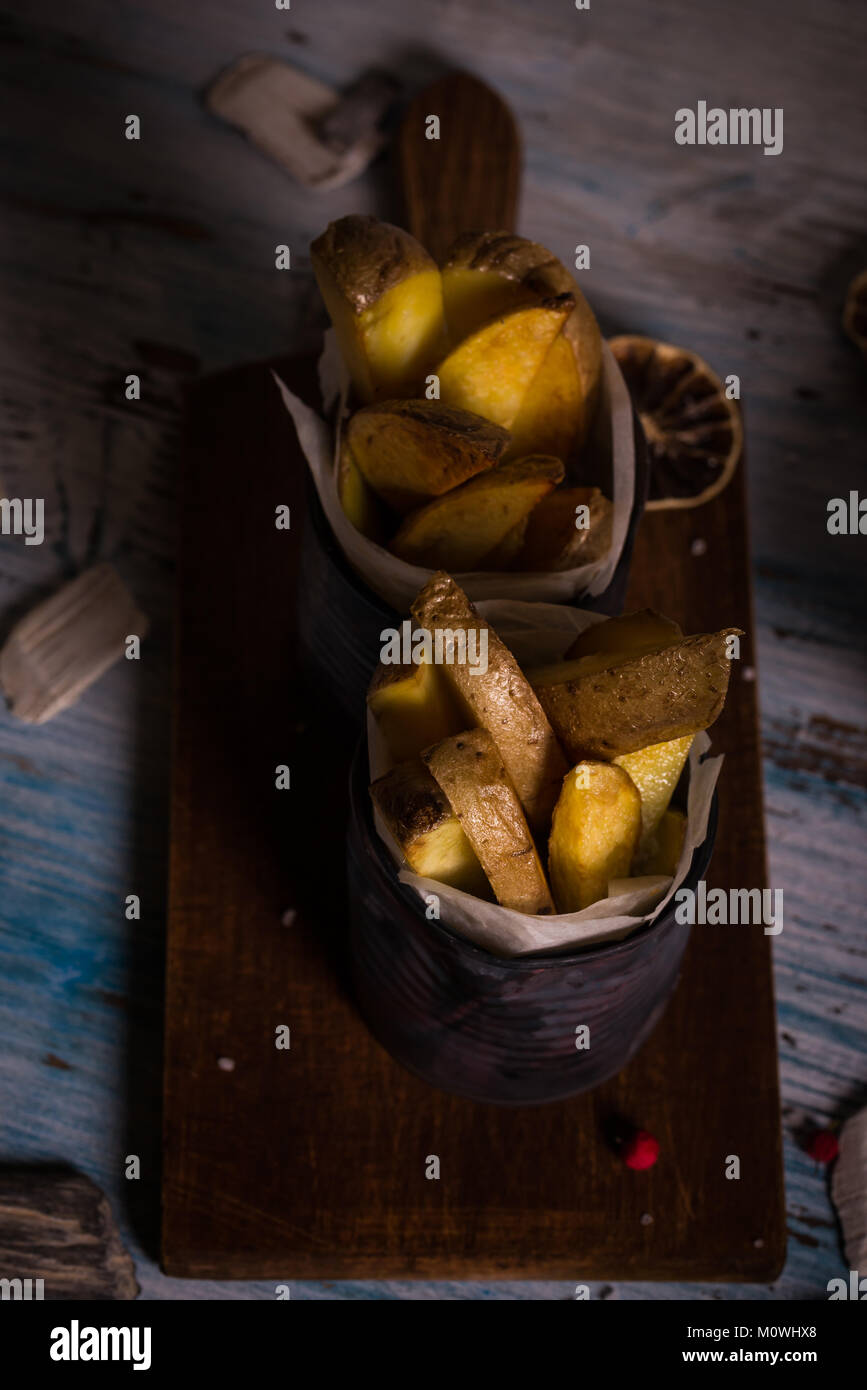 Vertical photo of two old vintage cans which are filled by paper and full of roasted potato strips. The potatoes are unpeeled with skin. Few berries a Stock Photo