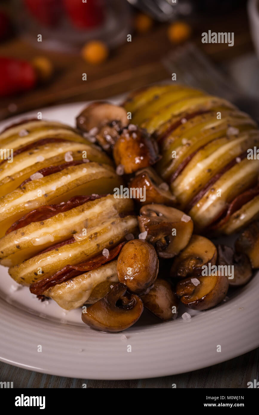 Vertical photo of fried potatoes. Two whole potatoes are sliced and grooves are filled by cheese, salami and bacon. Roasted mushrooms are spilled betw Stock Photo
