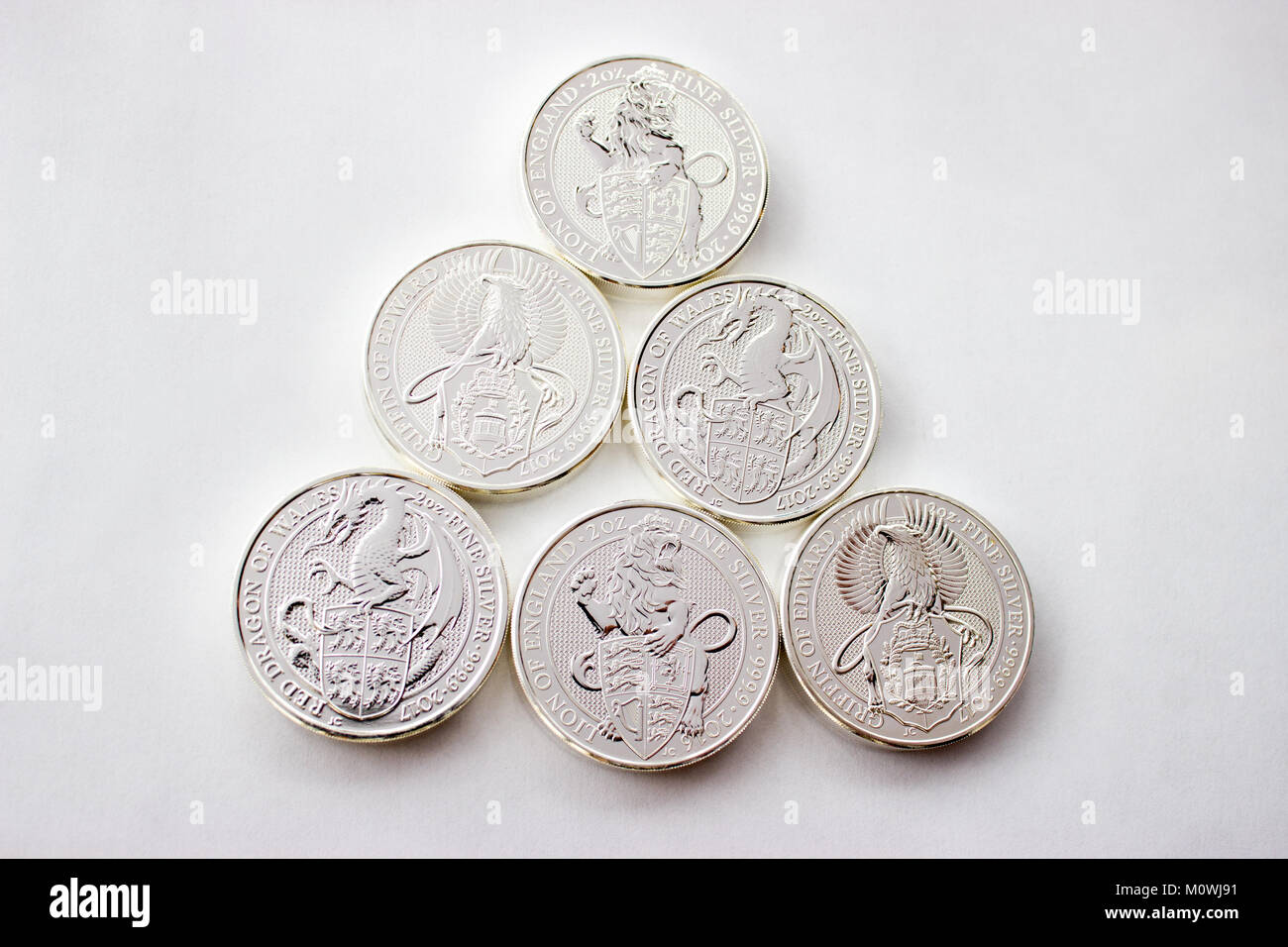 On a gray background are silver  coins of an investment silver from a British mints. Dragon of Wales, Lion of England and Griffin of Edward III. Stock Photo