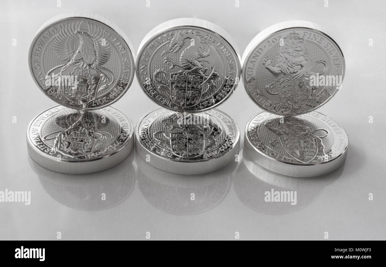 On a gray background are silver  coins of an investment silver from a British mints. Dragon of Wales, Lion of England and Griffin of Edward III. Stock Photo