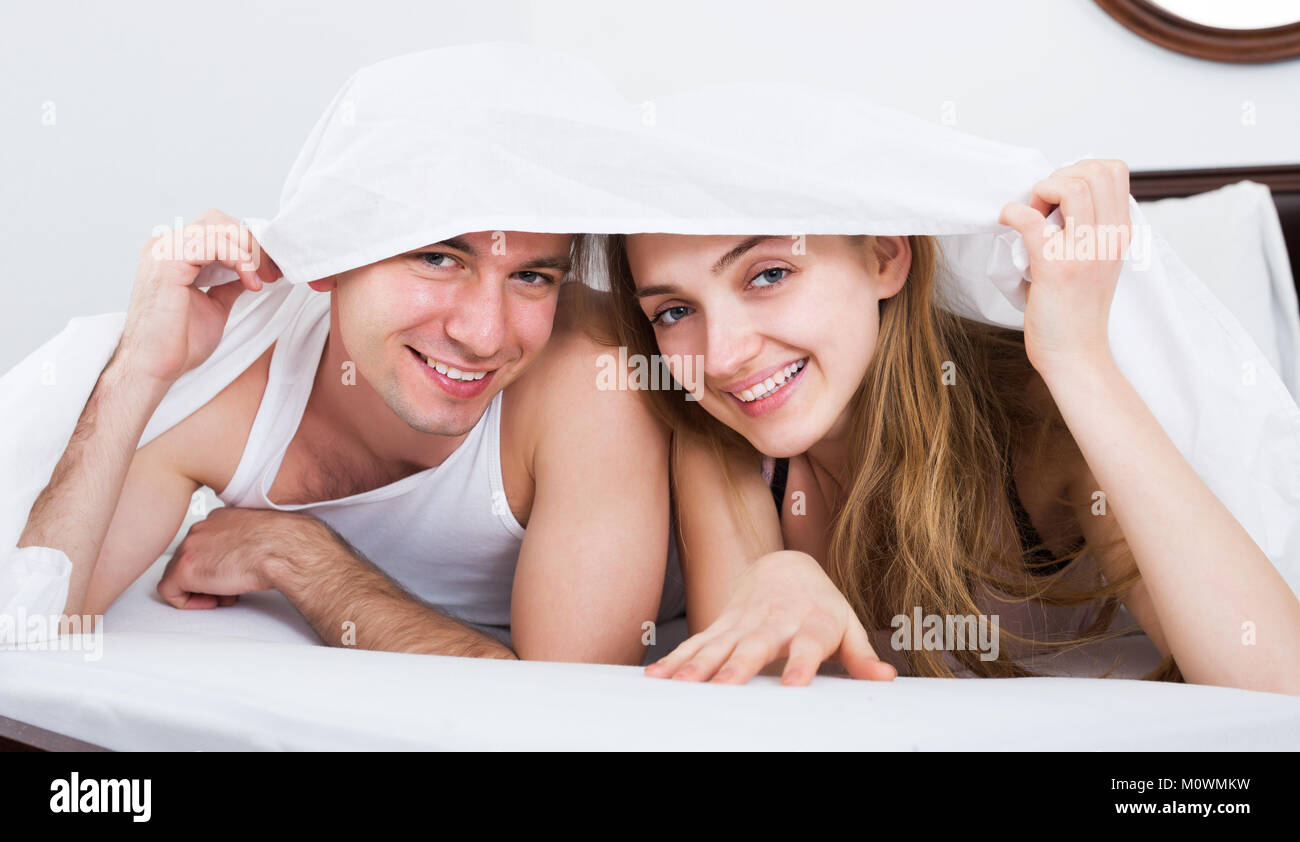 Happy young adults lying in family bed under sheet Stock Photo Alamy
