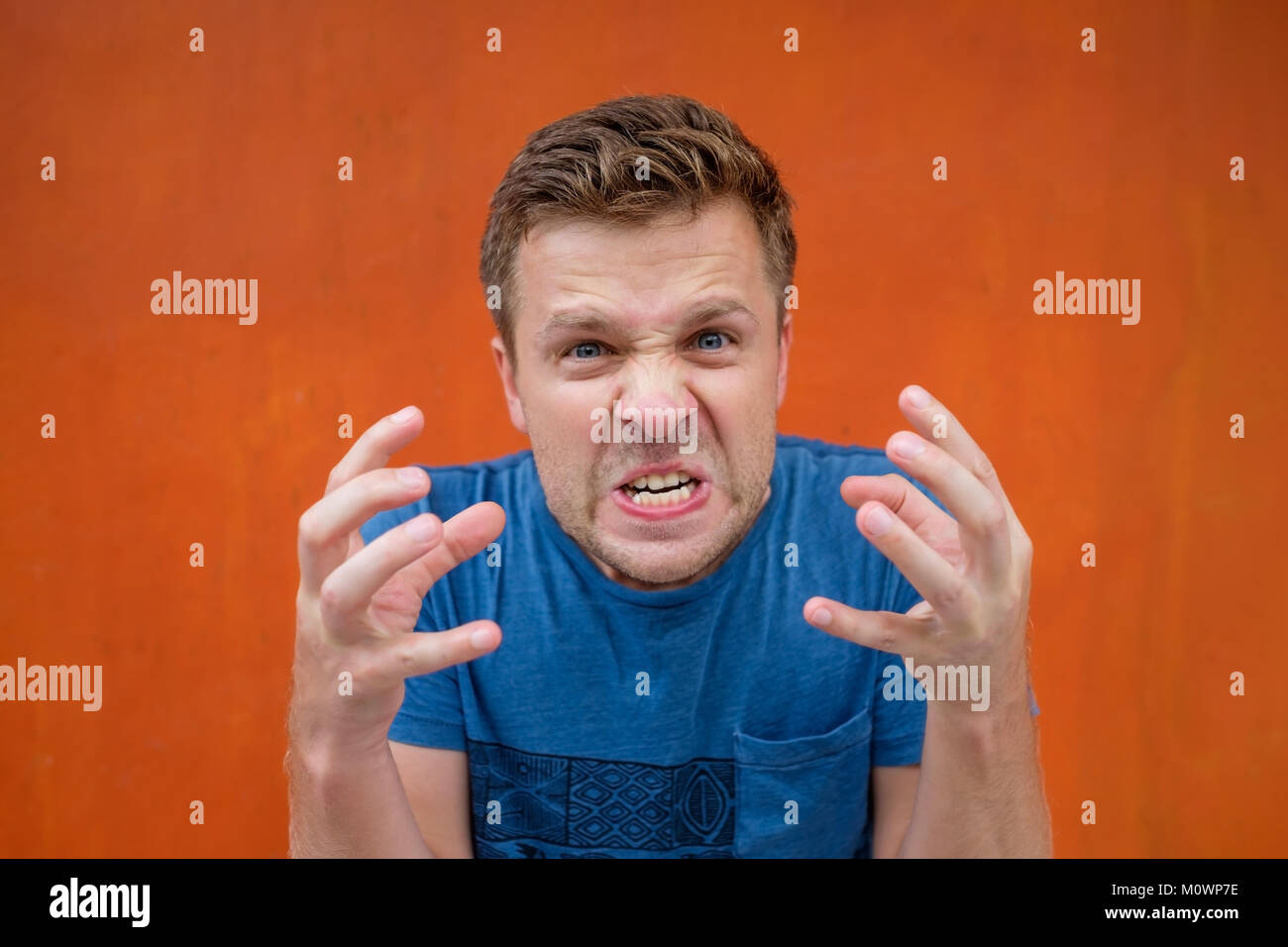 Desperate furious raged man in blue shirt screaming loudly having his eyes full of anger. Crazy evil boyfriend shouting at his girlfriend Stock Photo