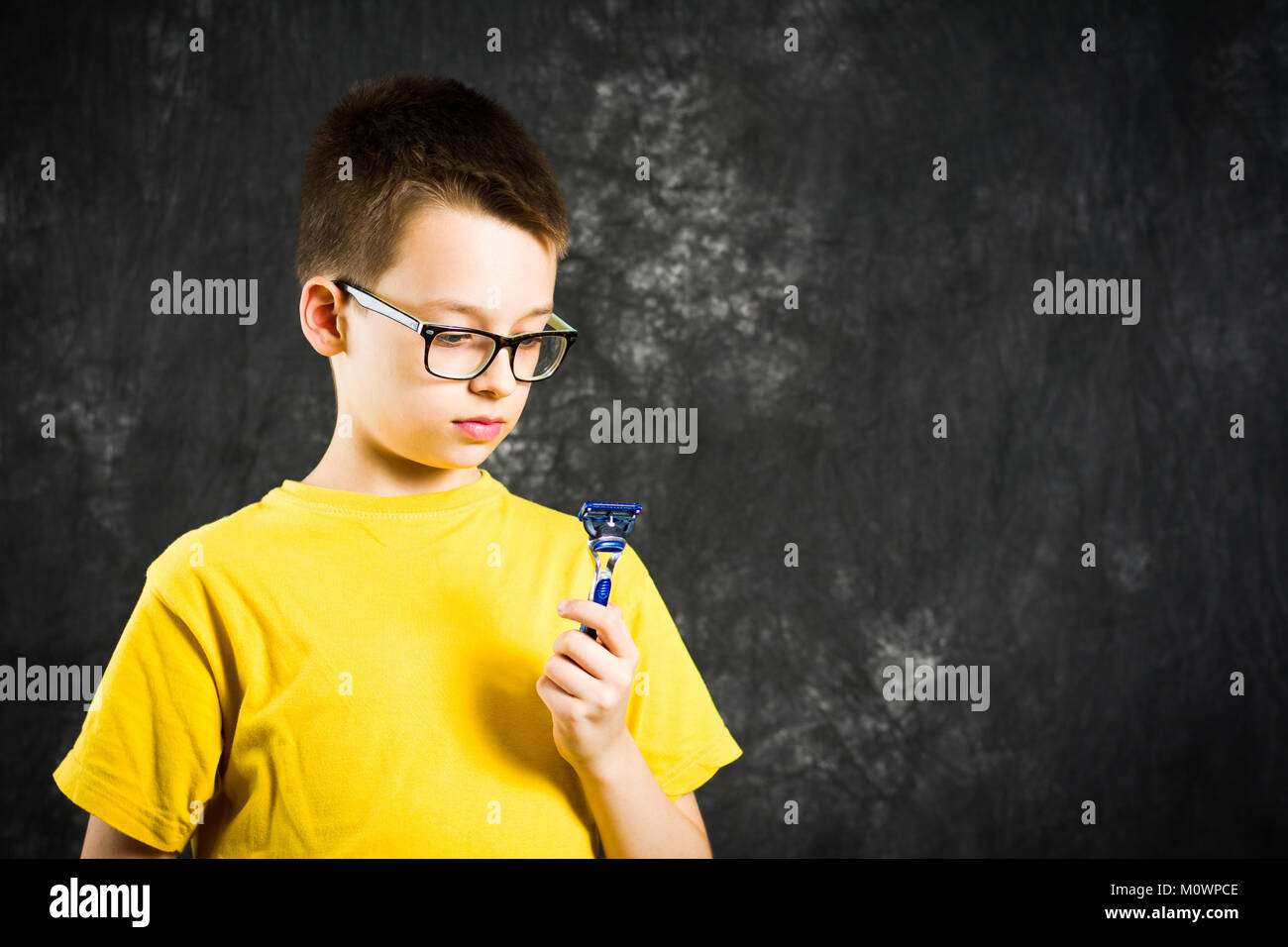 Teenage boy holding a shaver against dark background Stock Photo