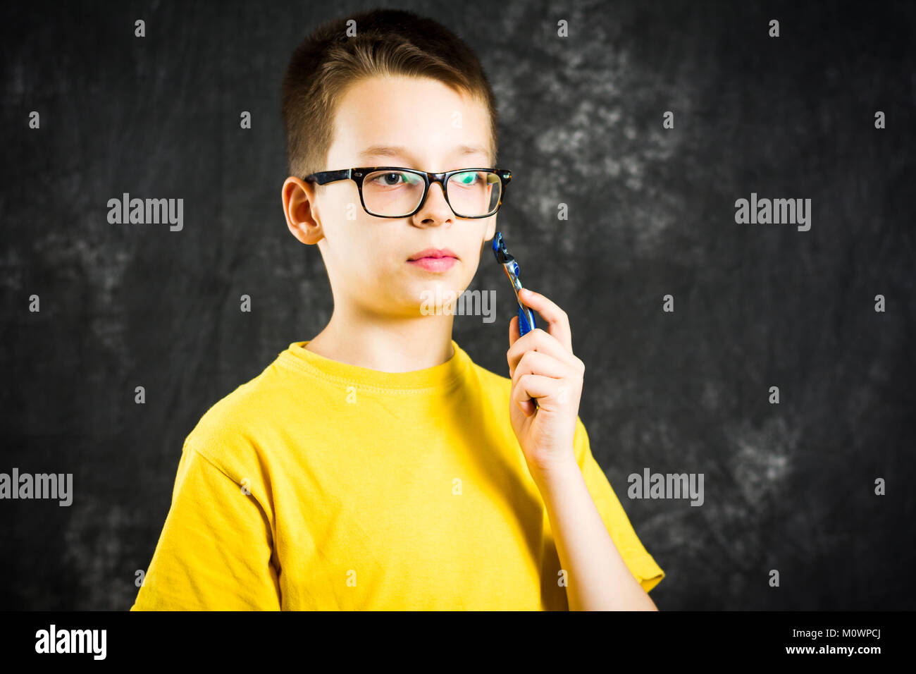 Teenage boy holding a shaver against dark background Stock Photo
