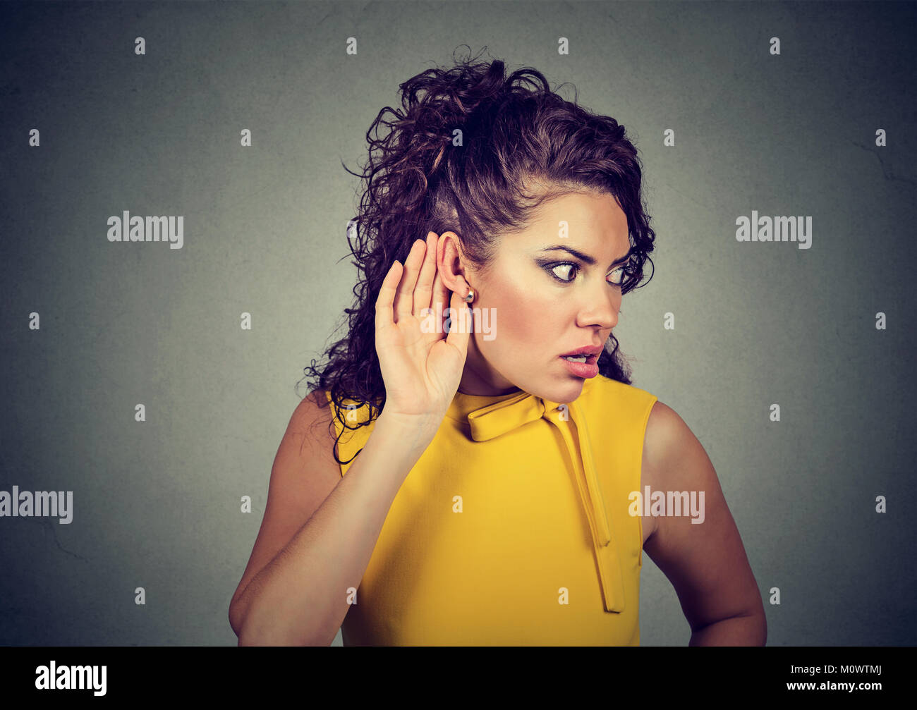 Young stylish woman spying and listening to gossip holding hand near ear. Stock Photo