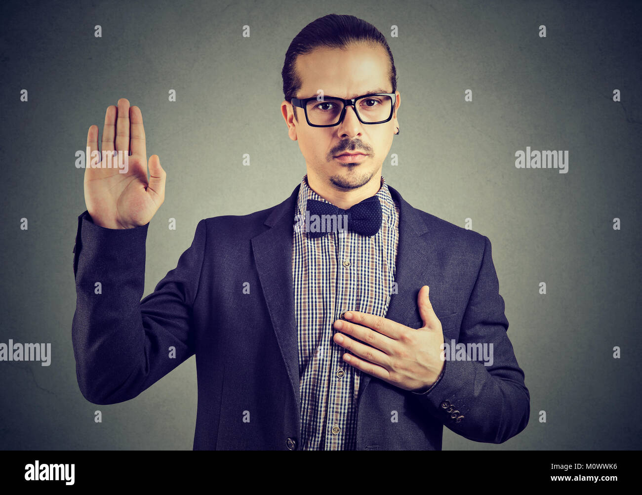 Young man in formal clothing and eyeglasses swearing in being trustworthy while looking at camera. Stock Photo
