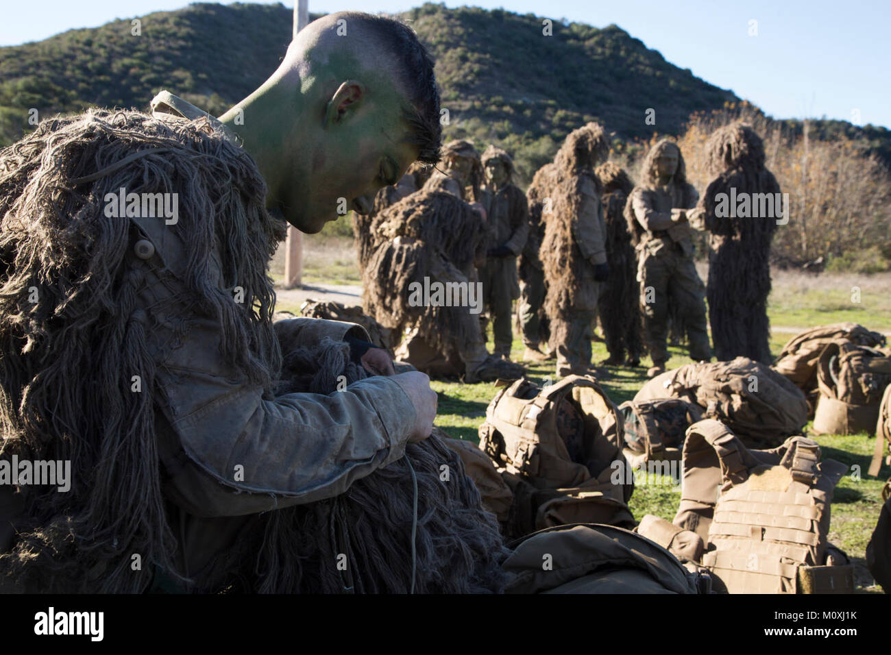 LCpl. Zachary Radack, 21, from Aliso Viejo, Calif., professionally instructed gunman with Regimental Surveillance and Target Acquisition Company, 1st Marine Regiment, adjusts his ghillie suit in preparation for a movement exercise on January 22, 2018. RSTAC is designed to build proficiency in scout sniper operations for service level exercises culminating in live fire full-mission profiles, reporting surveillance and reconnaissance control center operations and high-angle precision fires. (U.S. Marine Corps Stock Photo