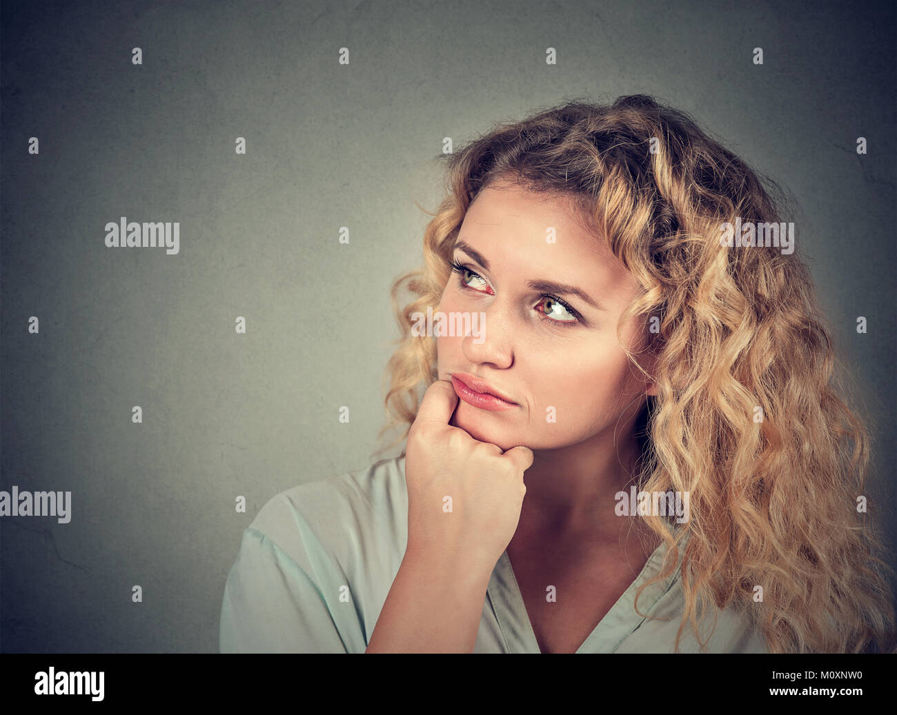 Young curly model looking away pensively while daydreaming on gray backdrop. Stock Photo