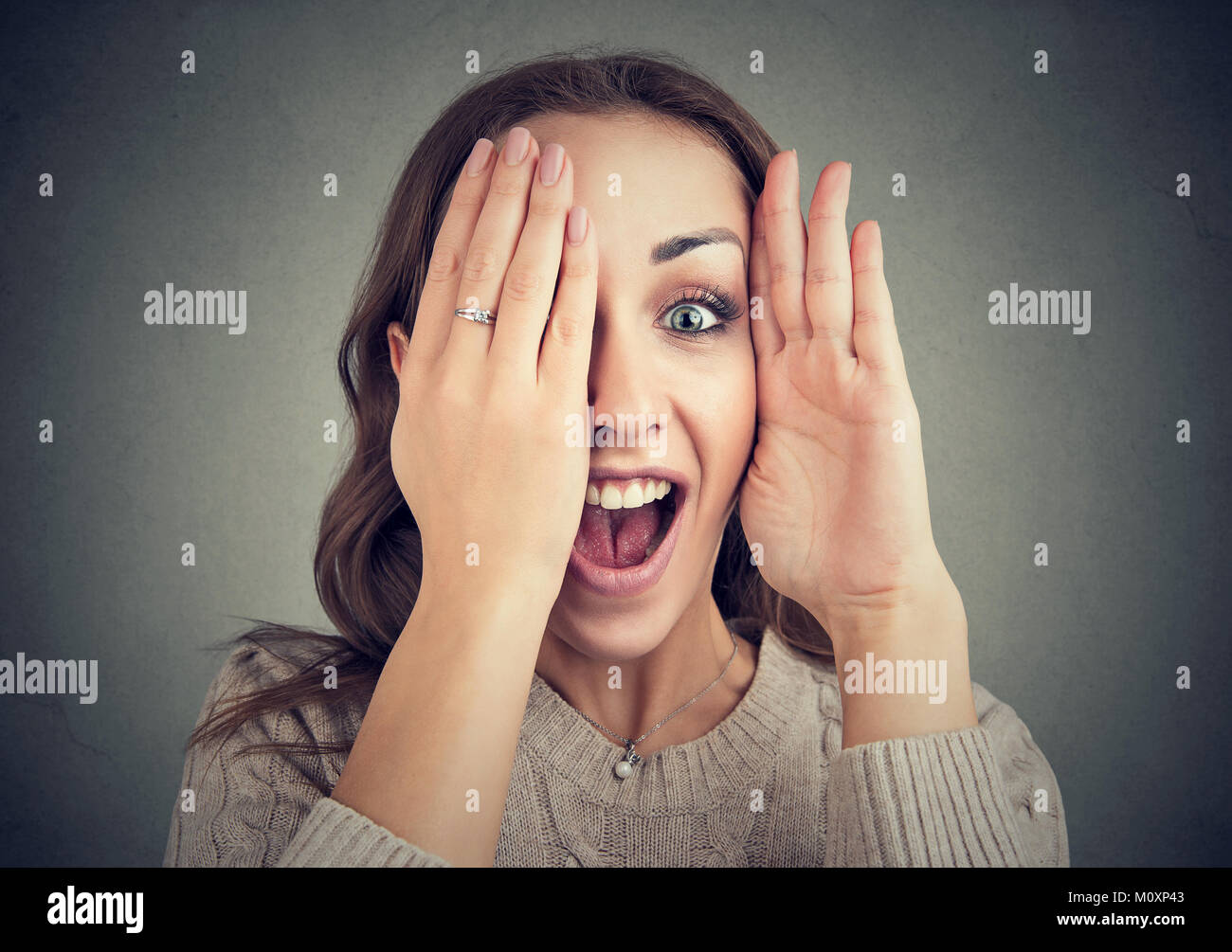 Portrait of young woman covering eye and looking at camera with funny