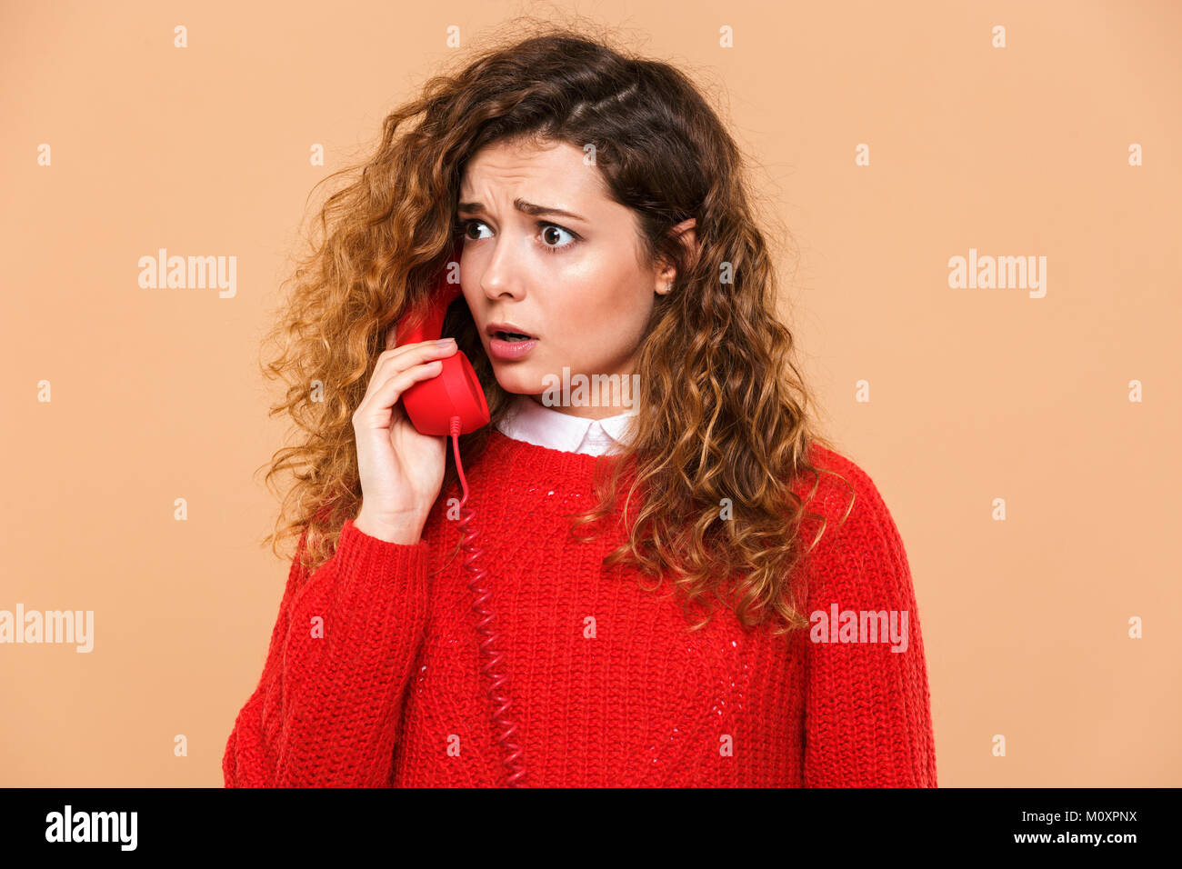 Portrait of an upset lovely girl talking on a landline telephone isolated over beige background Stock Photo