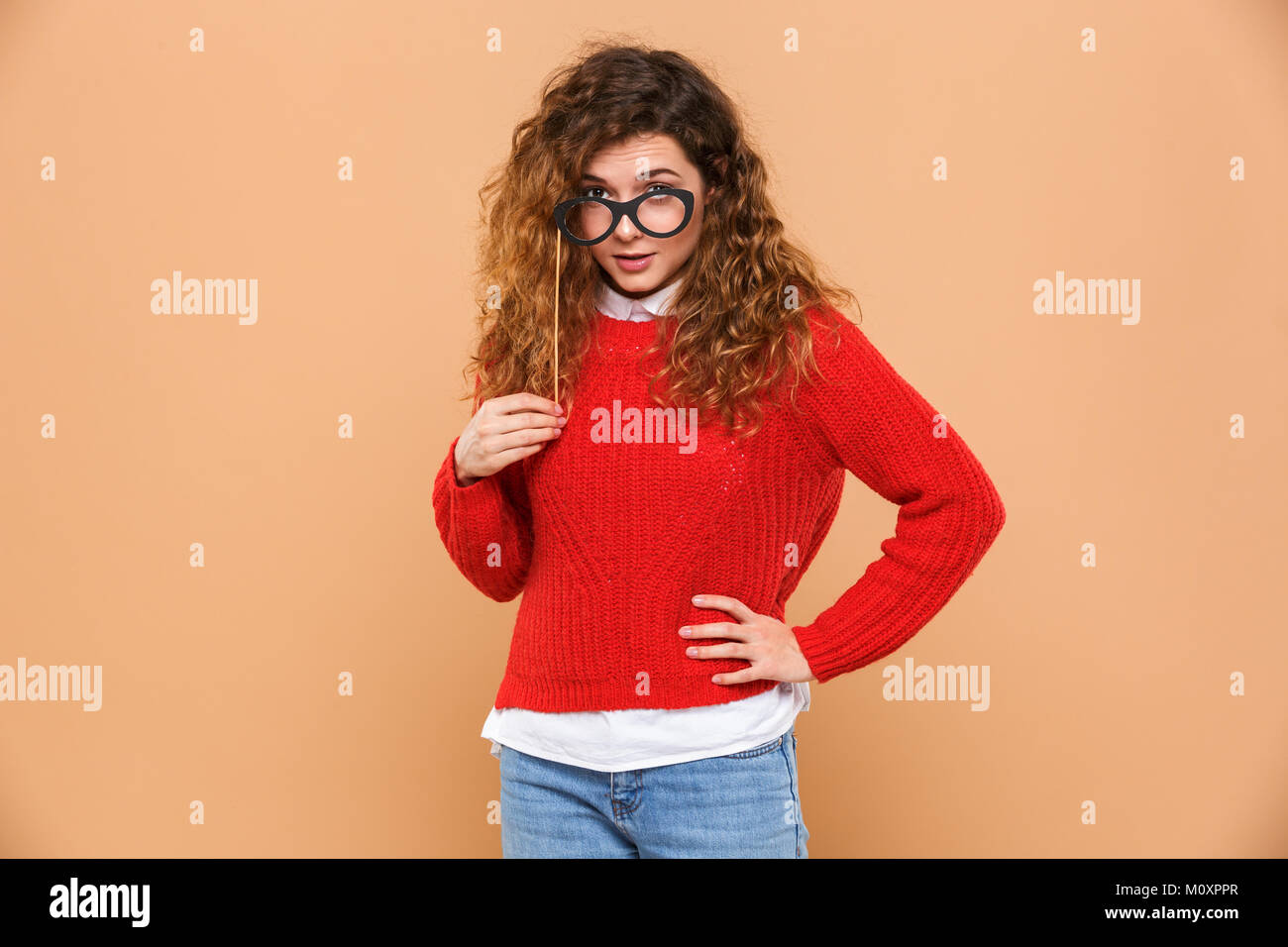 Portrait of a funny young girl holding fake eyeglasses at her face isolated over beige background Stock Photo