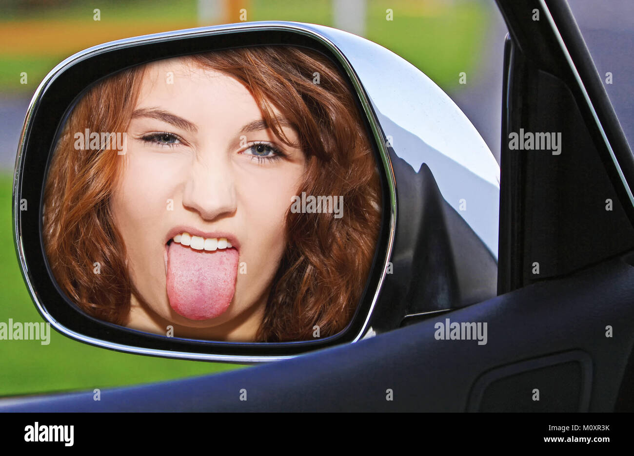 Young woman sticking tongue out in a side mirror of a car Stock Photo