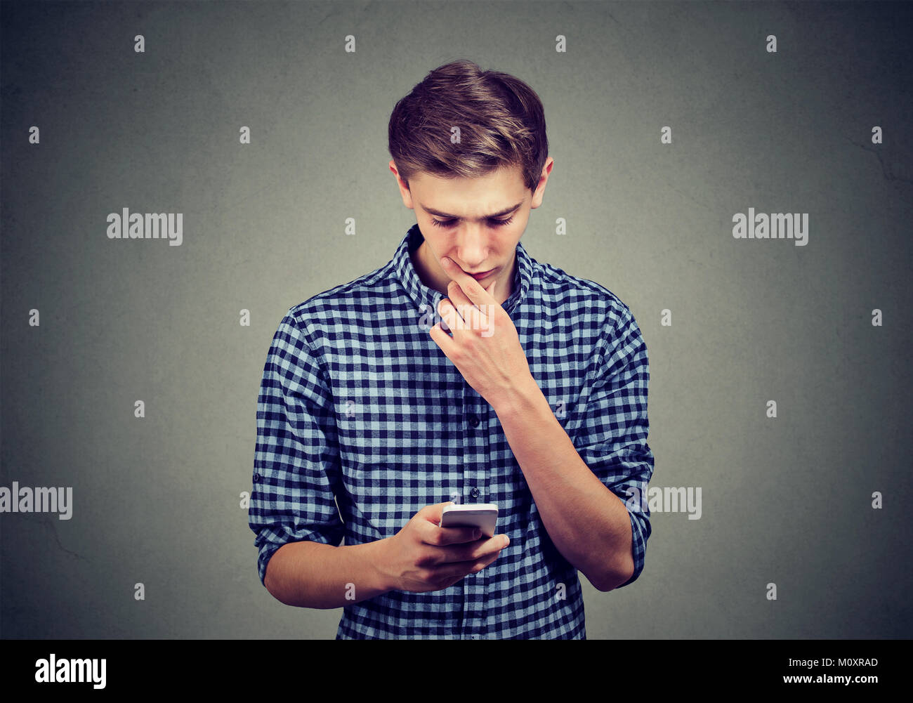 Casual teenager watching smartphone looking confused with complicated gadget. Stock Photo